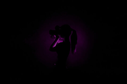 Center purple light silhouette on black background and lady photographer with camera taking photos. Concept of art photography. Dark violet  picture for website, avatar, Surreal abstract backdrop