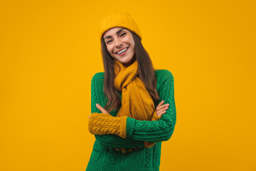 Close up portrait of beautiful young woman with charming smile posing in cozy knittet sweater, beanie hat, scarf and mittens isolated over yellow background.