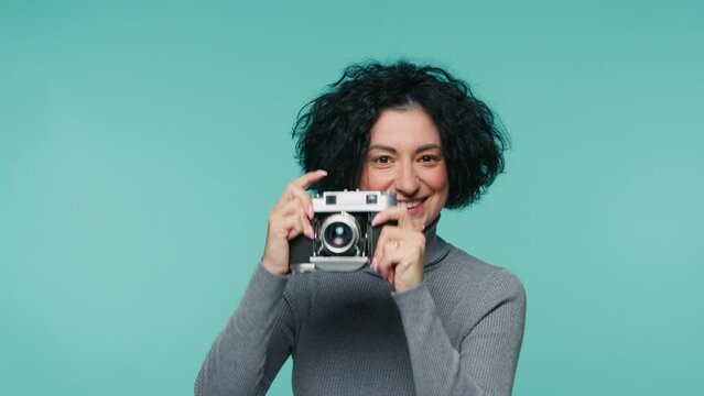 Waist up portrait of focused photographer with analog camera in teal blue photo studio on isolated background, looking at camera and viewfinder. Slow motion professional mature female photographer 4K