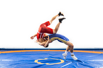 Two  strong men in blue and red wrestling tights are wrestlng and making a suplex wrestling on a yellow wrestling carpet