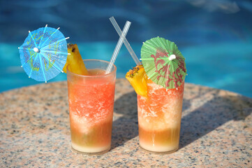 Two cocktail glasses by a poolside, blue water of swimming pool 
