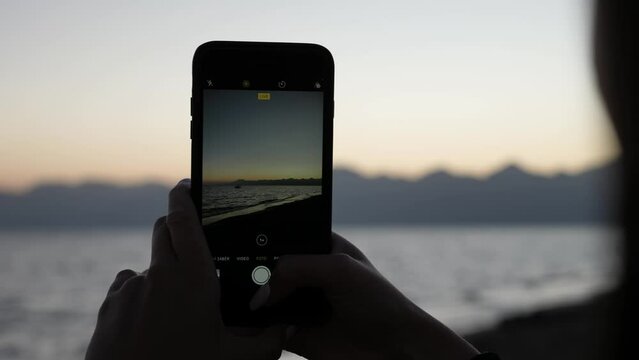 Female Hands Holding Smartphone and Taking Picture of Beautiful Sunset Above Mediterranean Sea, Close Up