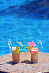 Fototapeta na wymiar Two cocktail glasses by a poolside, blue water of swimming pool, copy space