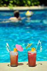 Obraz premium Two cocktail glasses left by a poolside, blue water of swimming pool, copy space
