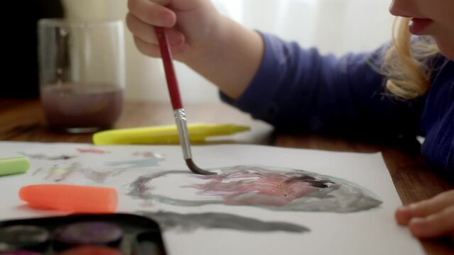 close up view of hand of unrecognizable girl who draws drawing on paper at home. Entertainment and hobbies of children, watercolor drawings on white sheet of paper. Hobby kid child at home.