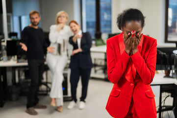 Young african woman crying because of the ridicule of colleagues. Racial discrimination in the...