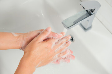 Hands of woman wash their hands in a sink with foam to wash the skin and water flows through the hands. Concept of health, cleaning and preventing germs and coronavirus from contacting hands