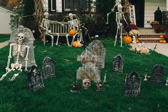  Many bright and colorful inflatable Halloween decorations, skeletons, carved pumpkins, and scarecrows in the driveway and front lawns of a residential house. High-quality photo