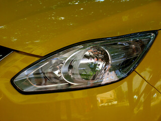 closeup view of silver color plastic headlight lens. yellow color shiny modern car. modern lighting technology. automobile. reflections of street scene on the yellow paint. car design concept. 