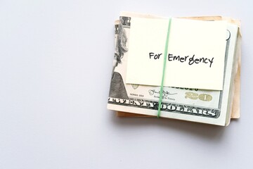 Dollars cash money and paper note with text written FOR EMERGENCY on copy space background - concept of financial planning saving money goal on purpose of rainy day crisis tough time