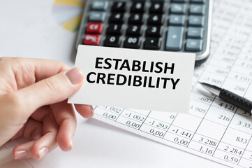 ESTABLISH CREDIBILITY text on a card in the hand of a businessman on the background of an office desk, a business concept