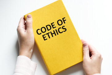Code of ethics words on a yellow notebook in the hands of a businessman on a light background. Business ethic concept.