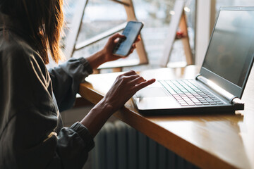 Young brunette woman in casual clothes working with laptop using mobile phone at cafe