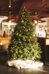 Blurred photo of Christmas tree decorated with garland of lights in public place in cafe or restaurant