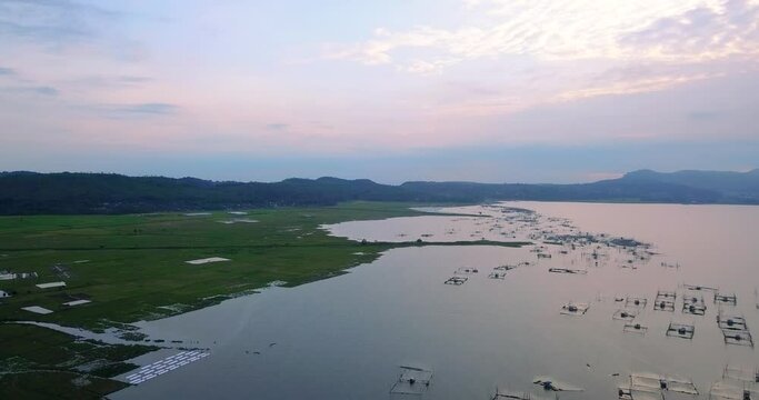 Aerial flyover view of fish cages and rice fields with mountains in background