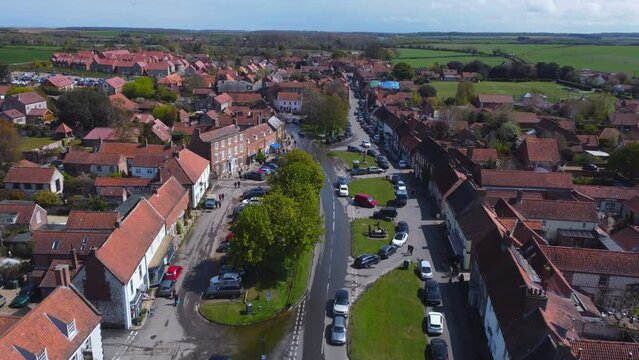 High Aerial Drone Shot Flying Over Beautiful Old Village Burnham Market with Red and White Houses on Sunny and Cloudy Day with People in the Streets in North Norfolk UK