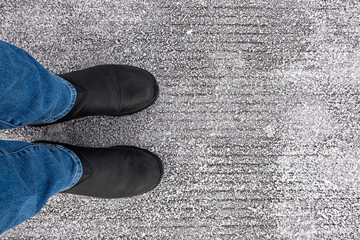 Top view of leather shoes standing on frosty road backgrounds. Person in blue jeans and boots...