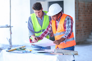 Two construction engineers holding blue print and inspecting the construction site