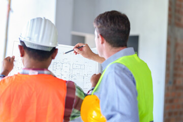 Two construction engineers holding blue print and inspecting the construction site