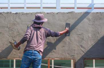 Rear view of builder worker using trowel to plastering cement on the wall inside of house...