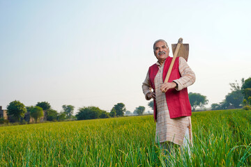 Indian farmer holding spade tool in hand and giving expression at agriculture field.