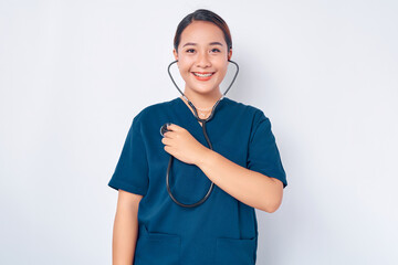 Smiling young Asian woman nurse wearing blue uniform with a stethoscope listens to his heartbeat, physician working in clinic isolated on white background. Healthcare medicine concept