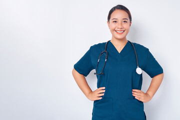 Smiling young Asian woman nurse wearing blue uniform with a stethoscope holding hands on her waist isolated on white background. Healthcare medicine concept