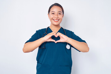 Smiling young Asian woman nurse wearing blue uniform with stethoscope showing heart gesture, caring...