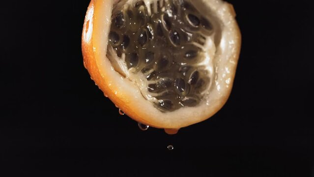 Slow Motion Macro Shot of Flowing Granadilla Juice from Halved Granadilla in black Background