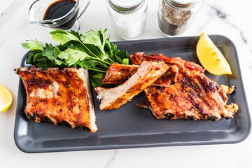 portioned grilled pork ribs on a rectangular ceramic plate with parsley and lemon slice. exquisite taste of food. menu.