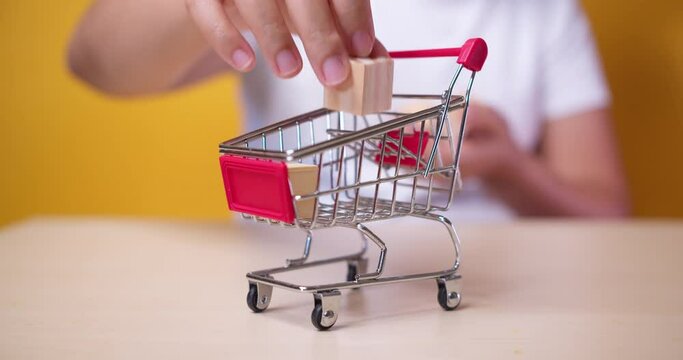 Hand-putting blank wooden cube mockup to Shopping trolley or cart for creative design copy space
