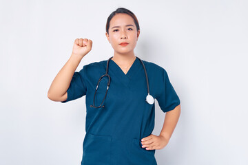 Serious young Asian woman nurse wearing blue uniform with a stethoscope showing support to fellow colleagues, raising fist in unity gesture isolated on white background. Healthcare medicine concept