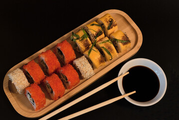 Delicious Japanese rolls with salmon, avocado, cucumber, cheese on wooden plate with wood sticks and soy sauce with selective focus on black background. Asian food concept. Healthy eating