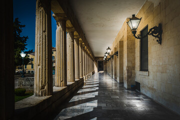 Covered walkway or stoa with Greek columns and lanterns at night.