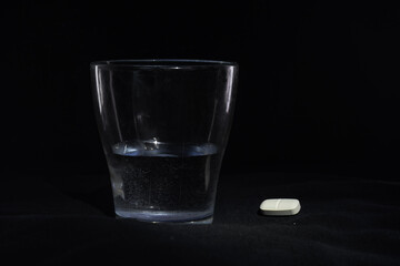 A tablet and a glass of water on a black background. The concept of health care and pharmaceuticals
