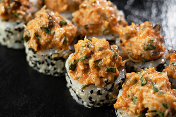 Fresh sushi rolls with salmon, avocado, mussels and black sesame seeds served on a black stone slate. Japanese sushi uramaki or California roll