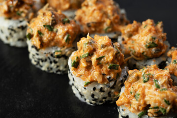 Set of fresh sushi rolls with salmon, avocado, mussels and black sesame seeds served on a black stone slate. Japanese sushi uramaki or California roll