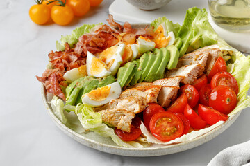 Cobb salad with grilled chicken, eggs, avocado, tomato, bacon on marble white background. Classic American salad, food. Healthy Keto diet.