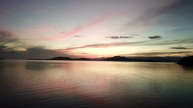Fishing boat sails by sea,Dramatic sunset over the sea and mountainous islands, clouds in the sky. View from small island Gili Asahan, near Lombok, Indonesia