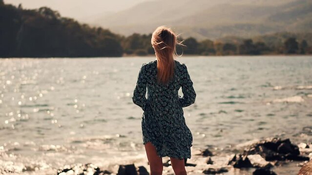 woman walks along ocean and hair flowing in sea breeze	
