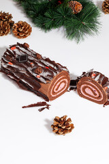 Sliced chocolate sponge cake roll with Christmas tree branch and gilded cones