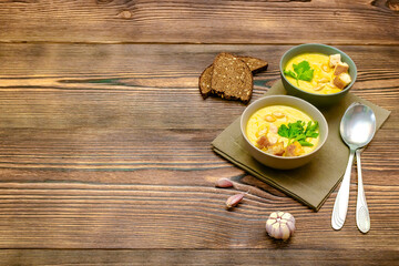 Vegetarian autumn pumpkin traditional soup with seeds, creamy silky texture, cilantro parsley dill greens, croutons, bread, garlic on wooden background. healthy vegan food concept, Top view