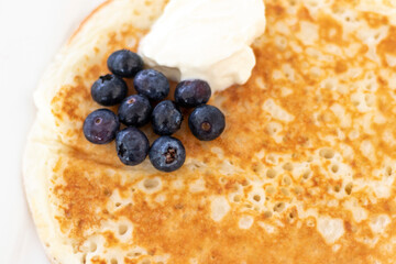 Close up shot of a pancake with sour cream and blueberries. Food