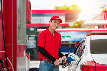 Asian attendant service male worker refuelling car at gas station. Smiling assistant man wear red uniform and red hat refuelling car at petrol station