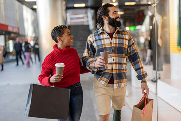 multiracial couple shopping in the city looking at window display, while carrying bags and coffee...