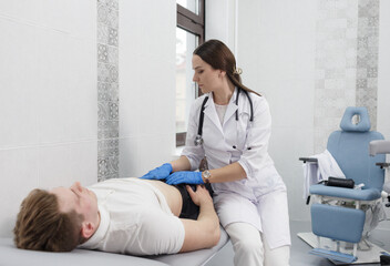 A focused young woman doctor conducting abdominal palpation in a middle-aged patient suffering from...