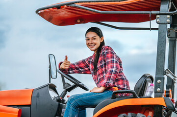 Asian young female farmer sitting on big tractor machine in farmland. Modern technologies in agriculture management and agribusiness concept. © Johnstocker