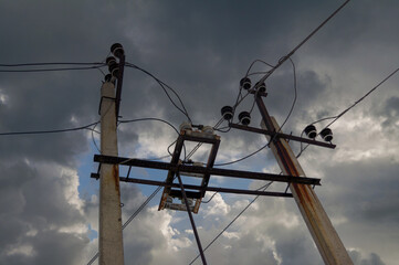 Mast of a high-voltage power line against the cloudy sky.