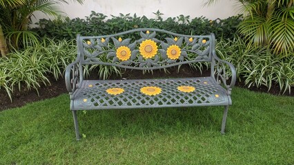 Old gray wrought iron bench in the garden with a decorative ornate metal legs and armrests. There is a flower-shaped decoration made of iron on the back side. Still in usable condition. Picture taken 