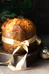 Italian Christmas cake, Panettoni decorated with golden bow on the wooden try at dark background   with Christmas tree and decoration